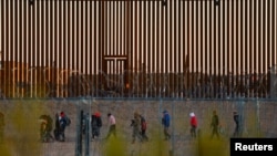 Migrants seeking asylum gather near the border wall after crossing a razor wire fence deployed to inhibit their crossing into the United States, as a member of the Texas National Guard escorts them, as seen from Ciudad Juarez, Mexico,Dec. 19, 2024. 