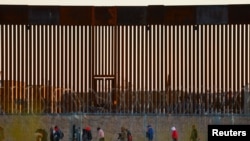 Migrants seeking asylum gather near the border wall after crossing a razor wire fence deployed to inhibit their crossing into the United States, as a member of the Texas National Guard escorts them, as seen from Ciudad Juarez, Mexico,Dec. 19, 2024. 