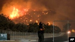 A sheriff's deputy stands guard at a gate near a hillside as the Holy Fire burns in the Cleveland National Forest at Temescal Valley in Corona, Calif., Aug. 9, 2018.