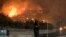 A sheriff's deputy stands guard at a gate near a hillside as the Holy Fire burns in the Cleveland National Forest at Temescal Valley in Corona, Calif., Aug. 9, 2018.