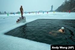 A man prepares to dive into a pool cut from the ice on top the frozen Songhua River while another person swims in the pool, January 7, 2025. (AP Photo/Andy Wong)