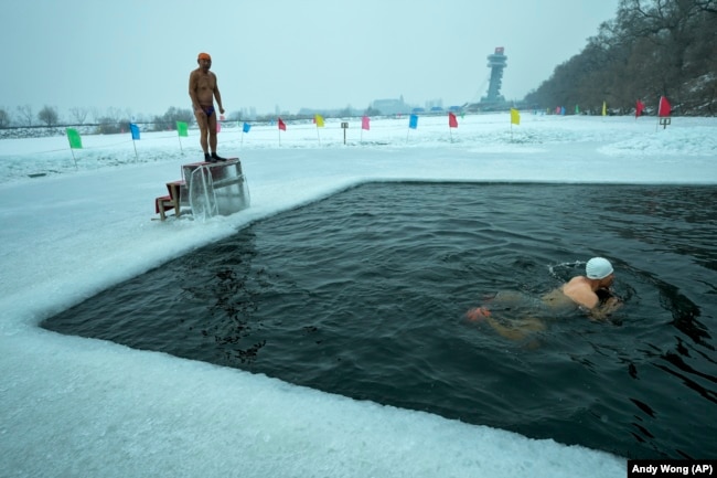 A man prepares to dive into a pool cut from the ice on top the frozen Songhua River while another person swims in the pool, January 7, 2025. (AP Photo/Andy Wong)