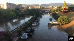 Cars are piled as others remain trapped in water and mud after an underpass, seen in the background, flooded on Wednesday in the Sicilian city of Palermo, southern Italy, as seen early on July 16, 2020.
