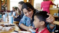 FILE - Wendlin Giron talks with her son, Uziel Enoc Banegas Giron, 5, as they eat a complimentary lunch at a Share a Meal event for homeless families hosted at a local restaurant by the Miami Police Department, Dec. 13, 2016, in Miami. Giron is an immigrant from Honduras who was granted political asylum in the U.S.