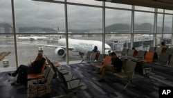 FILE - Travelers wait at a departure area as an aircraft operated by Cathay Pacific Airways taxis at Hong Kong International Airport, in Hong Kong, Oct. 8, 2023.