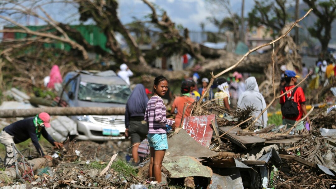 Para korban berdiri di antara reruntuhan akibat topan Haiyan di Tacloban, Filipina Tengah, 8 Desember 2013. FIFA menawarkan bantuan $1 Juta untuk perbaikan lapangan sepakbola akibat topan itu. 