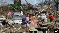 Para korban berdiri di antara reruntuhan akibat topan Haiyan di Tacloban, Filipina Tengah, 8 Desember 2013. FIFA menawarkan bantuan $1 Juta untuk perbaikan lapangan sepakbola akibat topan itu. 