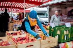 A saleswoman takes apples from a crate at a weekly market in Germany, March, 20, 2020 in Hanover, Germany.