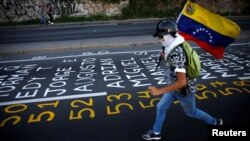 FILE - A demonstrator carries a Venezuelan flag as he runs next to a list of the victims of the violence during protests against Venezuela's president Nicolas Maduro government in Caracas, June 12, 2017.