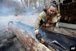 In this Thursday, Nov. 15, 2018, photo, Mashpee Wampanoag Phillip Wynne, of Sagamore, Mass., pours water to control fire and temperatures while making a mishoon, a type of boat, from a tree at the Wampanoag Homesite at Plimoth Plantation, in Plymouth.