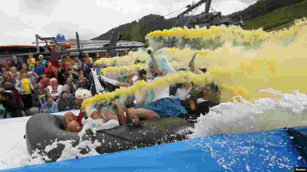 Para peserta menahan jilatan api sementara meluncur di atas pelampung di sepanjang jalur perosotan yang mengarah ke kolam air dan busa dalam festival &quot;Letniy Gornoluzhnik&quot; di the Bobroviy Log Fun Park dekat kota Siberia Krasnoyarsk, Rusia.