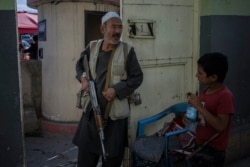 A boy looks at the rifle of a guard from a Shiite Hazara minority outside a mosque in Kabul, Nov. 10, 2021.