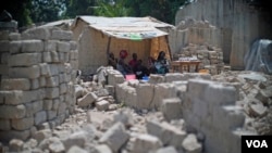 A family uses tarps taken from a refugee camp to get shelter from the sun, with bricks for rebuilding their homes all around them in the PK5 neighborhood of Bangui, Feb. 2017. (Z. Baddorf/VOA)