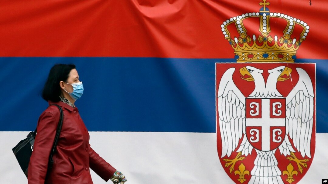 Žena sa maskom na licu hoda pored državne zastave Republike Srbije pre početka zabrane kretanja, tokom vanrednog stanja zbog epidemije koronavirusa u Srbiji (AP Photo/Darko Vojinović)