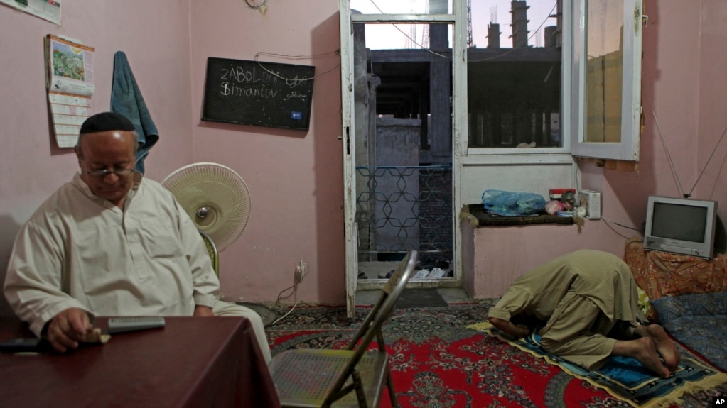 افغانستان میں آخری یہودی زیبولان سائمنٹوو سیناگاگ میں واقع اپنے گھر میں بیٹھے ہیں، ان کا مسلمان دوست قریب ہی نماز پڑھ رہا ہے (ایسوسی ایٹڈ پریس، 29 مئی 2009 کی تصویر)