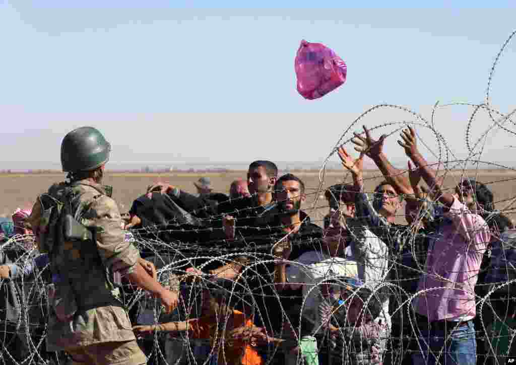 A Turkish soldier throws a bag of bottled water toward the Syrian refugees who were waiting at the border in Suruc, Turkey, Sept. 21, 2014. 