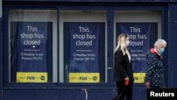 People wearing face masks walk past a closed retail unit in Preston, Britain, March 9, 2021. Europeans are hopeful that U.S. President Joe Biden's stimulus package will benefit their struggling economies, too. 