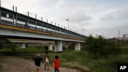 FILE - Migrant children walk with their families along the Rio Grande, as pedestrian commuters use the Puerta Mexico bridge to enter Brownsville, Texas, seen from Matamoros, Tamaulipas state, Mexico, June 26, 2019.