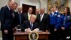 President Donald Trump signs a policy directive to send American astronauts back to the moon, and eventually Mars, in the Roosevelt Room of the White House, Dec. 11, 2017, in Washington.