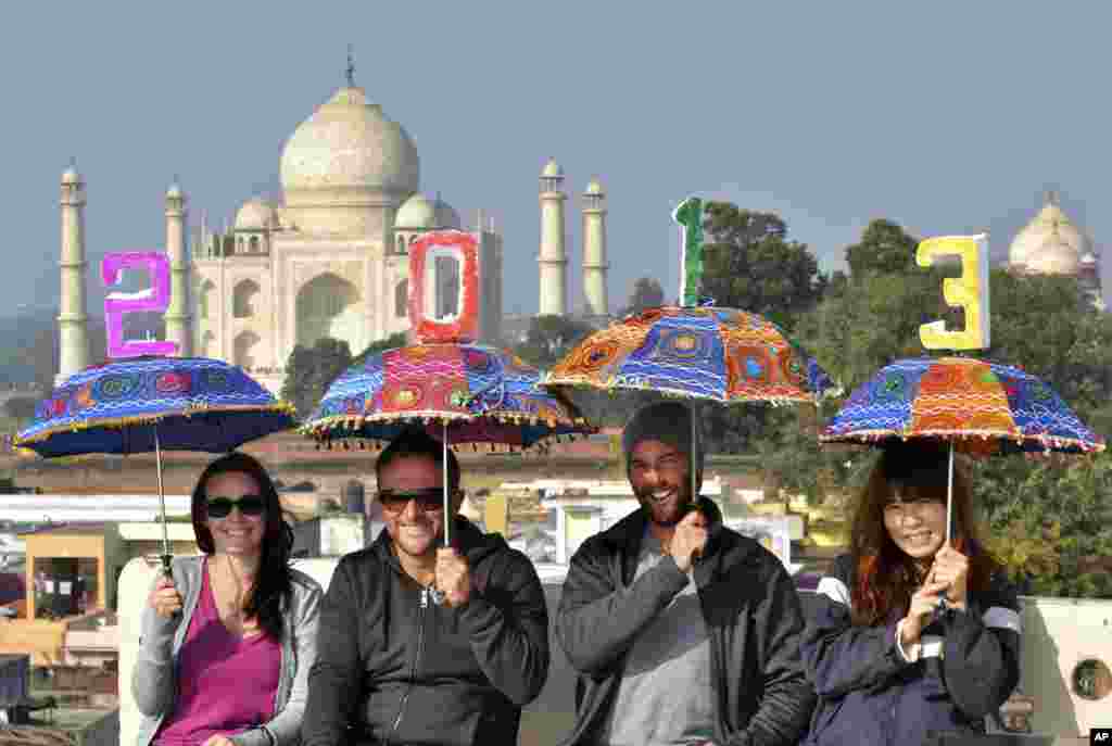 Tourists pose as they carry umbrellas with numbers to welcome the new year on the terrace of a hotel near the Taj Mahal in Agra, India, December 31, 2012. 