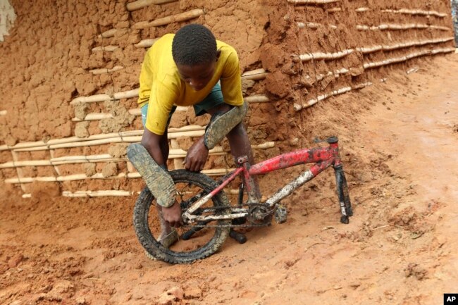 A young boy inspects part of a bicycle retrieved from a site where two houses were crushed by the collapse of a massive, sprawling dumpsite in Pemba city on the northeastern coast of Mozambique, Monday, April, 29, 2019.