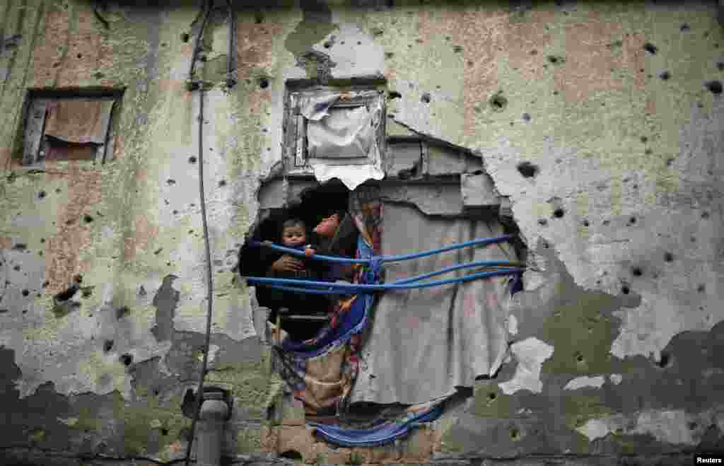 Palestinian children look out through a hole covered with a blanket in their family house, that witnesses said was damaged by Israeli shelling during a 50-day war last summer, in the east of Gaza City.