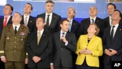 French President Emmanuel Macron, front center, speaks with German Chancellor Angela Merkel, front second right, as they look up at a drone flying above their heads during a group photo at an EU summit at the Europa building in Brussels, Dec. 14, 2017.