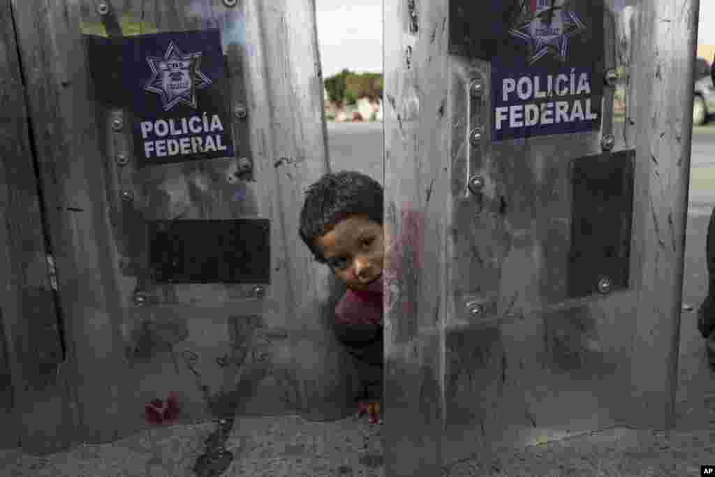 Elias Lopez, a three-year-old Honduran migrant, plays in between the shields of a line of Mexican riot police, when the group he was part of tried to cross the Chaparral border crossing in Tijuana, Mexico, Nov. 22, 2018. 