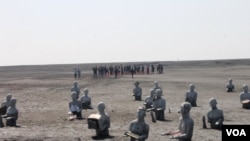 Patung penyintas dengan latar belakang warga penyintas yang melakukan ziarah makam leluhur, Minggu, 24 Mei 2015. (VOA/Petrus Riski)