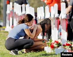 A student at Marjory Stoneman Douglas High School weeps in front of makeshift memorials set up for shooting victims while a fellow classmate consoles her at the school, in Parkland, Florida, Feb. 18, 2018.