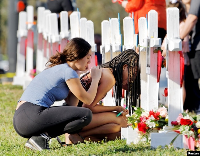 FILE - A student at Marjory Stoneman Douglas High School weeps in front of a cross and Star of David for a shooting victim while a fellow classmate consoles her at a memorial by the school in Parkland, Florida, Feb. 18, 2018.