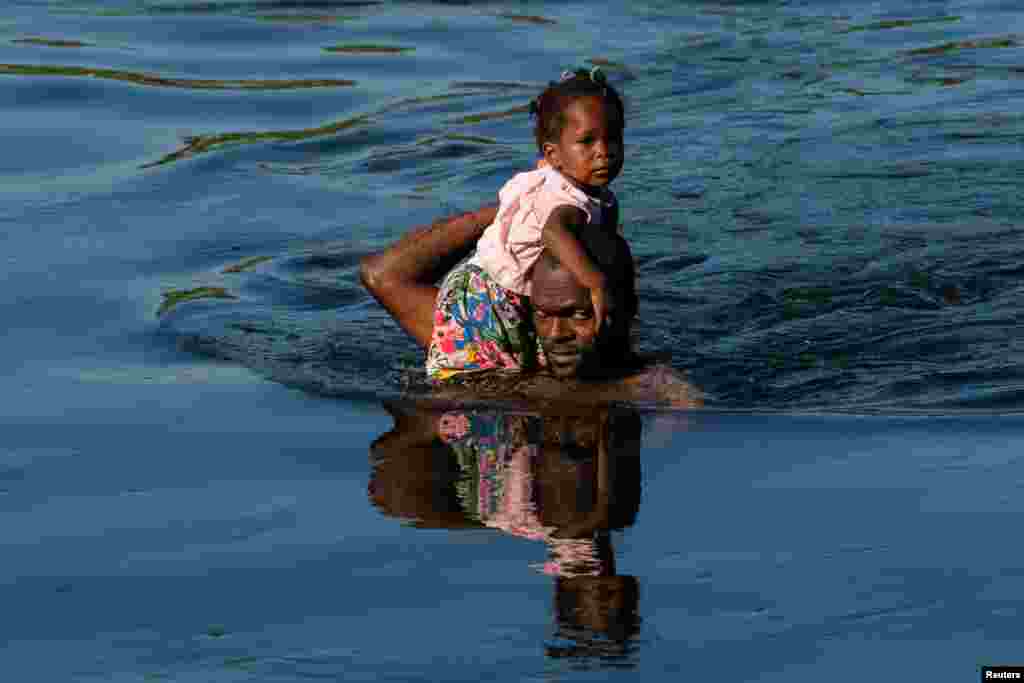 An asylum-seeking migrant carrying a girl, crosses the Rio Grande river towards Mexico near the International Bridge between Mexico and the U.S. in Ciudad Acuna, Mexico, Sept. 19, 2021.