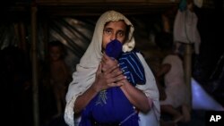 In this Nov. 26, 2017, photo, Jamila Begum, 35, caresses a favorite shirt and school bag of her late son who was killed by members of Myanmar's armed forces accused of massacring civilians in in Myanmar's Rakhine State.