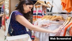 Woman with bag looking through clothes in shopping mall