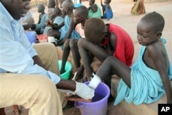 FILE - Ajak Kuol Nyamchiek watches while John Lotiki, a nurse with the Carter Center, bandages blisters on her leg from where a guinea worm is emerging, Abuyong, Sudan, Nov. 4, 2010.