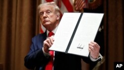 President Donald Trump holds up a signed Executive Order on hiring American workers, during a meeting with U.S. tech workers, in the Cabinet Room of the White House, Monday, Aug. 3, 2020, in Washington.(AP Photo/Alex Brandon)