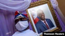 A man stands next to a portrait of slain Haitian President Jovenel Moise placed on a memorial at the city hall in Cap-Haitien, Aug. 22, 2021.