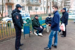 A Russian police officer wearing a face mask to protect against coronavirus, speaks to a group of people, some of them wearing face masks, as he patrols an area at an apartment building in Moscow, April 11, 2020.