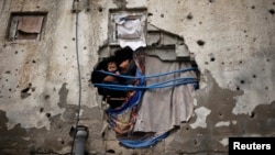 Palestinian children look out through a hole covered with a blanket in their family house, that witnesses said was damaged by Israeli shelling during a 50-day war last summer, in the east of Gaza City January 7, 2015. Heavy rains and near-freezing tempera