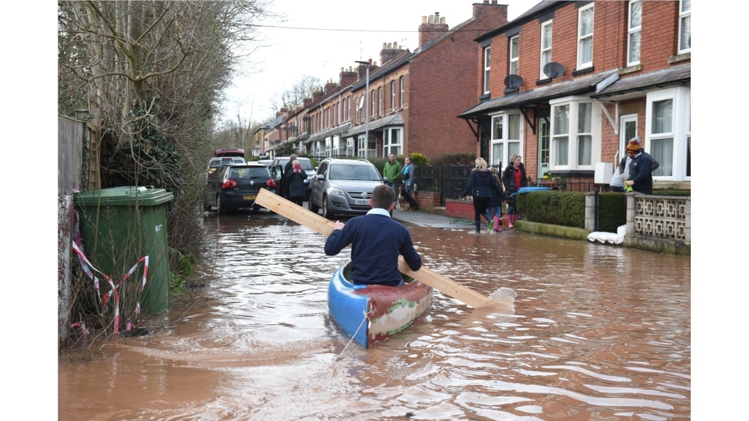 A man uses a plank of wood to paddle a kayak on floodwater after the River Wye burst its banks in Ross-on-Wye, western England, Feb. 17, 2020, in the aftermath of Storm Dennis.