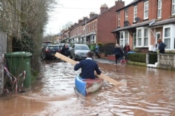A man uses a plank of wood to paddle a kayak on flood water after the River Wye burst its banks in Ross-on-Wye, western England, on February 17, 2020, in the aftermath of Storm Dennis.