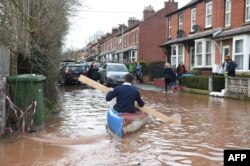 A man uses a plank of wood to paddle a kayak on flood water after the River Wye burst its banks in Ross-on-Wye, western England, on February 17, 2020, in the aftermath of Storm Dennis.