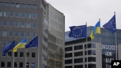 Bendera Uni Eropa dan Ukraina berkibar tertiup angin di depan spanduk untuk menandai peringatan tahun ketiga invasi Rusia ke Ukraina di luar markas besar Uni Eropa di Brussels, 24 Februari 2025. (Foto: AP/Virginia Mayo)