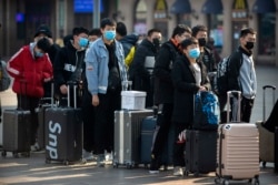 Travelers wear face masks as they stand outside the Beijing Railway Station in Beijing, Jan. 31, 2020.