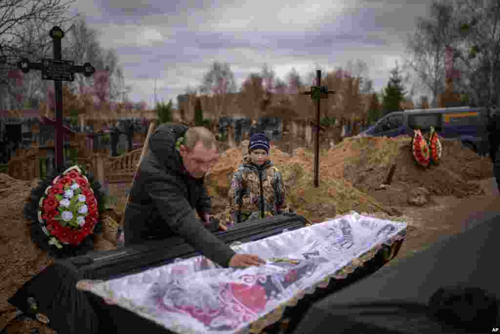 Vova, 10, looks at the body of his mother, Maryna, lying in a coffin as his father, Ivan Drahun, prays during her funeral in Bucha, on the outskirts of Kyiv, Ukraine.