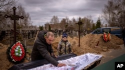 کودک ١٠ ساله اوکراینی و پدرش در کنار تابوت حامل جنازه مادرش؛ قبرستان بوچا در حومه کی‌یف، پایتخت اوکراین. ٢٠ آوریل ٢٠٢٢