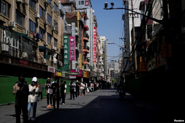 Warga berdiri di jalan menunggu tes asam nukleat saat lockdown di tengah pandemi COVID-19, di Shanghai, China, 17 April 2022. (REUTERS/Aly Song)