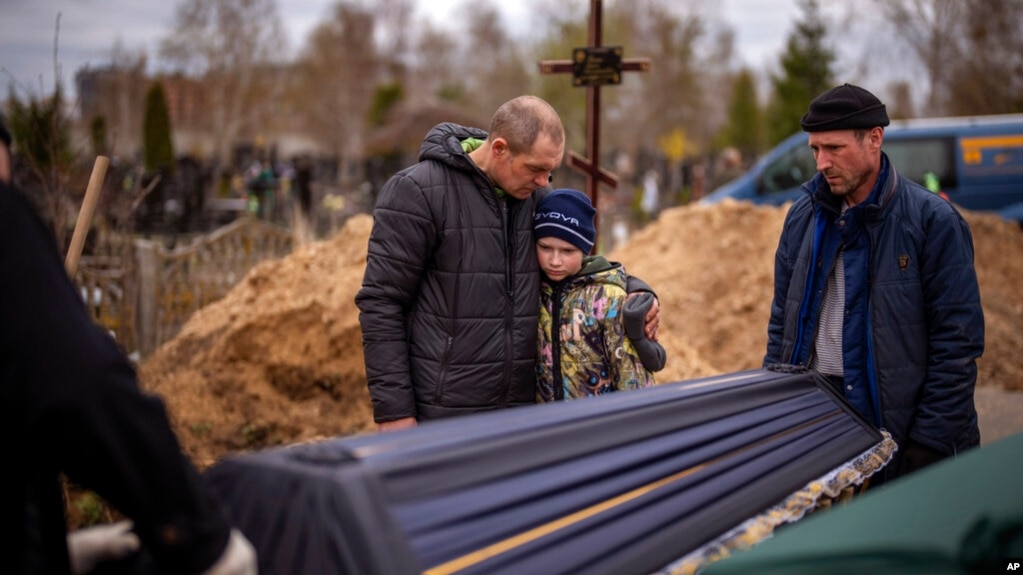 Vova, 10, looks at the coffin carrying body of his mother, Maryna, as his father, Ivan Drahun, hugs him during her funeral in Bucha, on the outskirts of Kyiv, April 20, 2022.