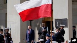 Defense Secretary Lloyd Austin, right, stands with Polish Defense Minister Mariusz Błaszczak, left, as the National Anthem is played during an arrival ceremony at the Pentagon in Washington, Apr. 20, 2022.