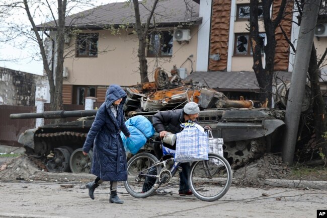 Local civilians walk past a tank in an area controlled by Russian-backed separatist forces in Mariupol, Ukraine, Tuesday, April 19, 2022.